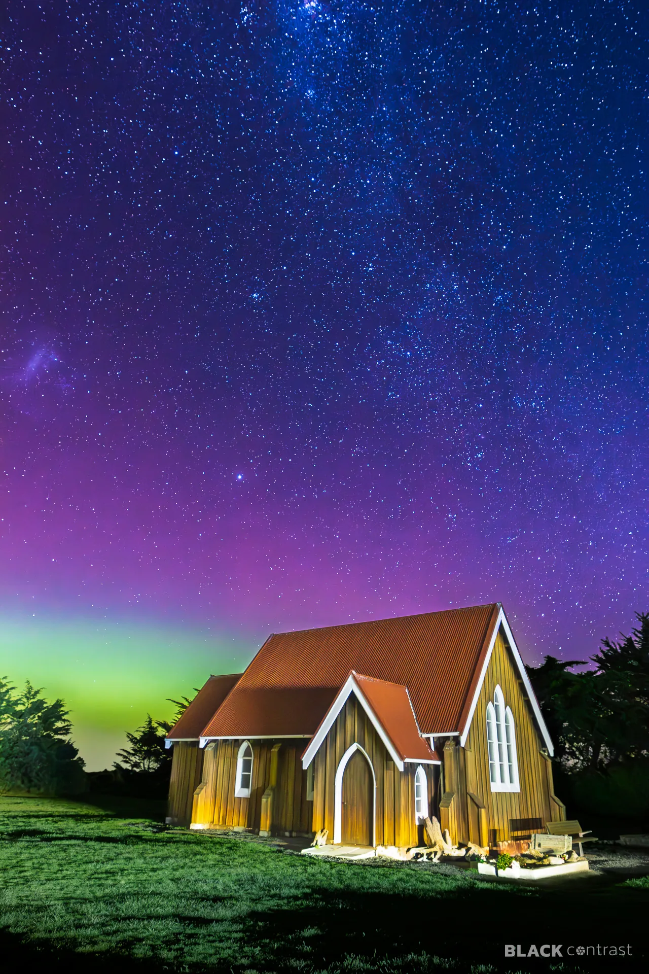 Wooden church beneath the aurora australis and a star-filled night sky
